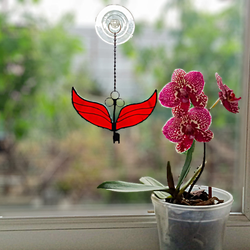 Stained glass fantasy winges key decoration hanging next to a potted orchid plant indoors.