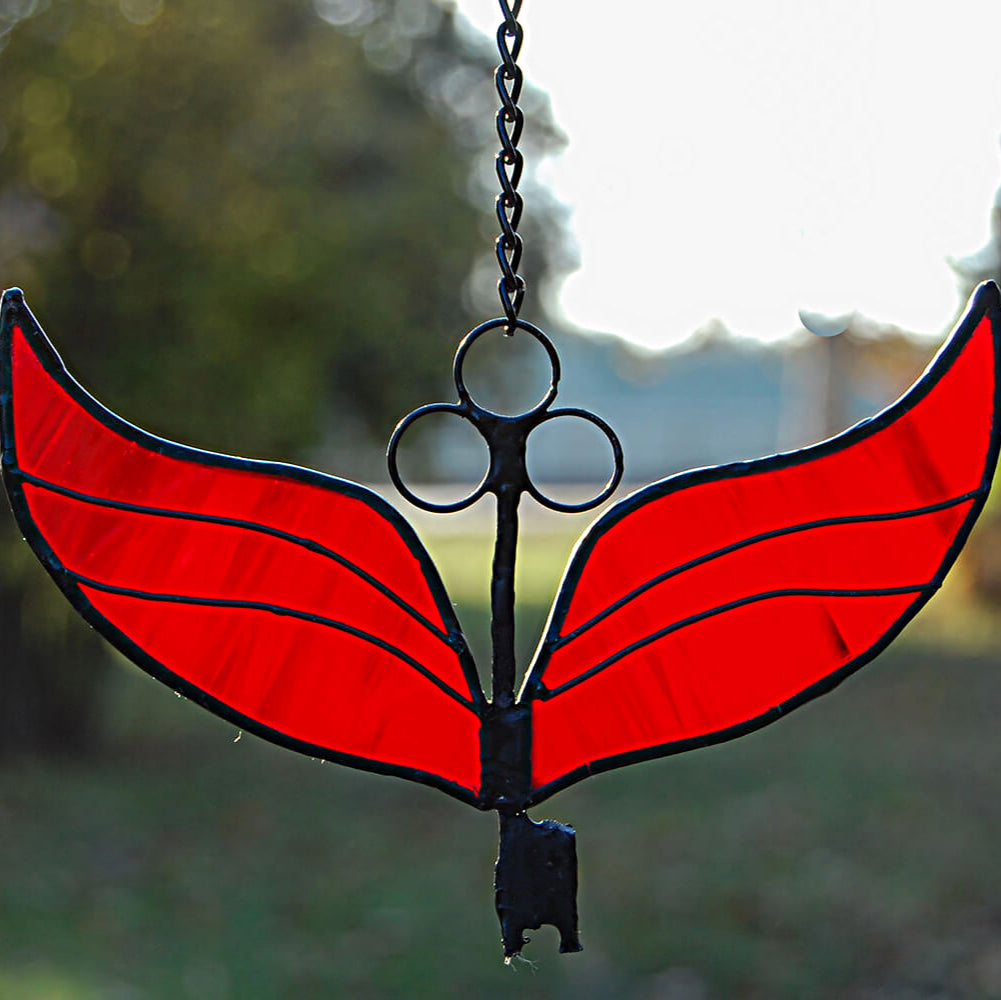 Stained glass red winged design hanging against a blurred natural background
