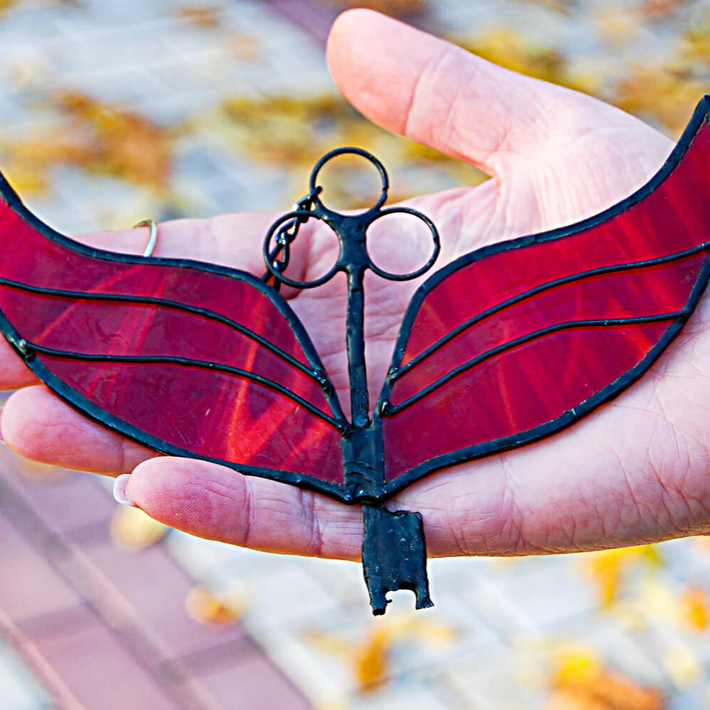 Hand holding a red and black butterfly-shaped keychain with blurred autumn leaves in the background