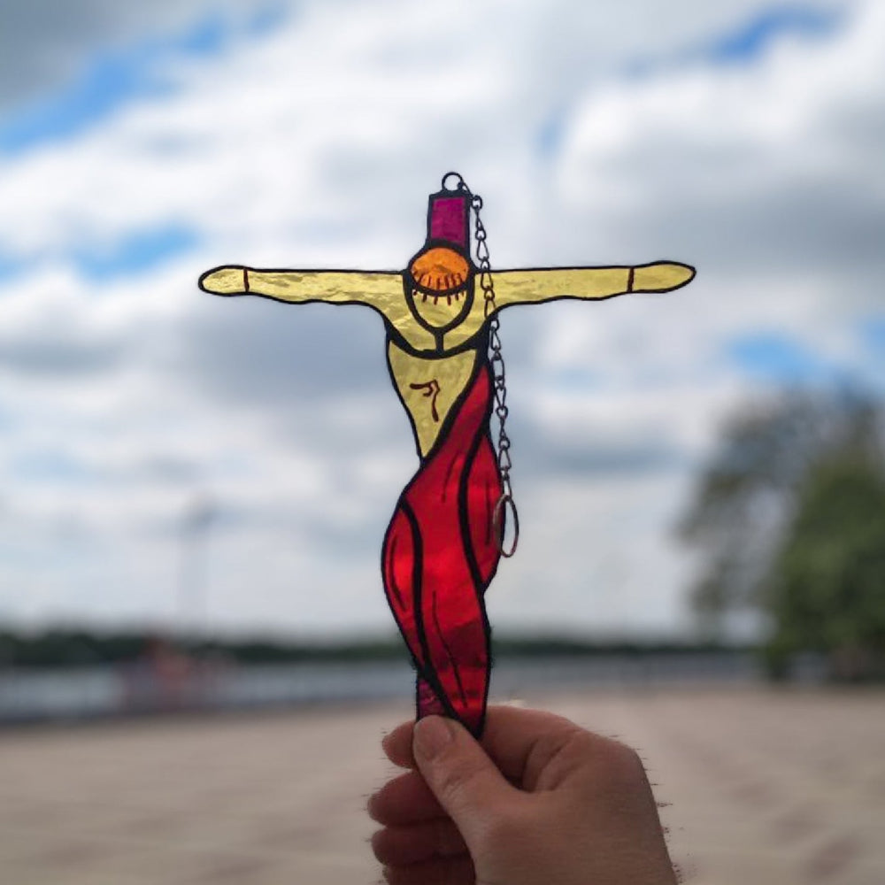 Stained glass crucifixion suncatcher with red drapery held up against a cloudy sky