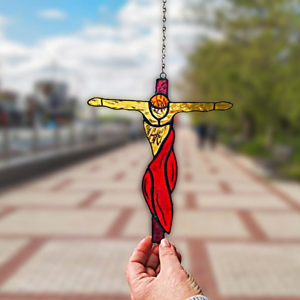 Hand holding a stained glass crucifixion suncatcher with red drapery outdoors near a riverside path