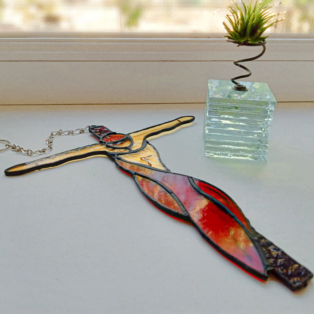 Stained glass crucifixion suncatcher with red drapery on windowsill
